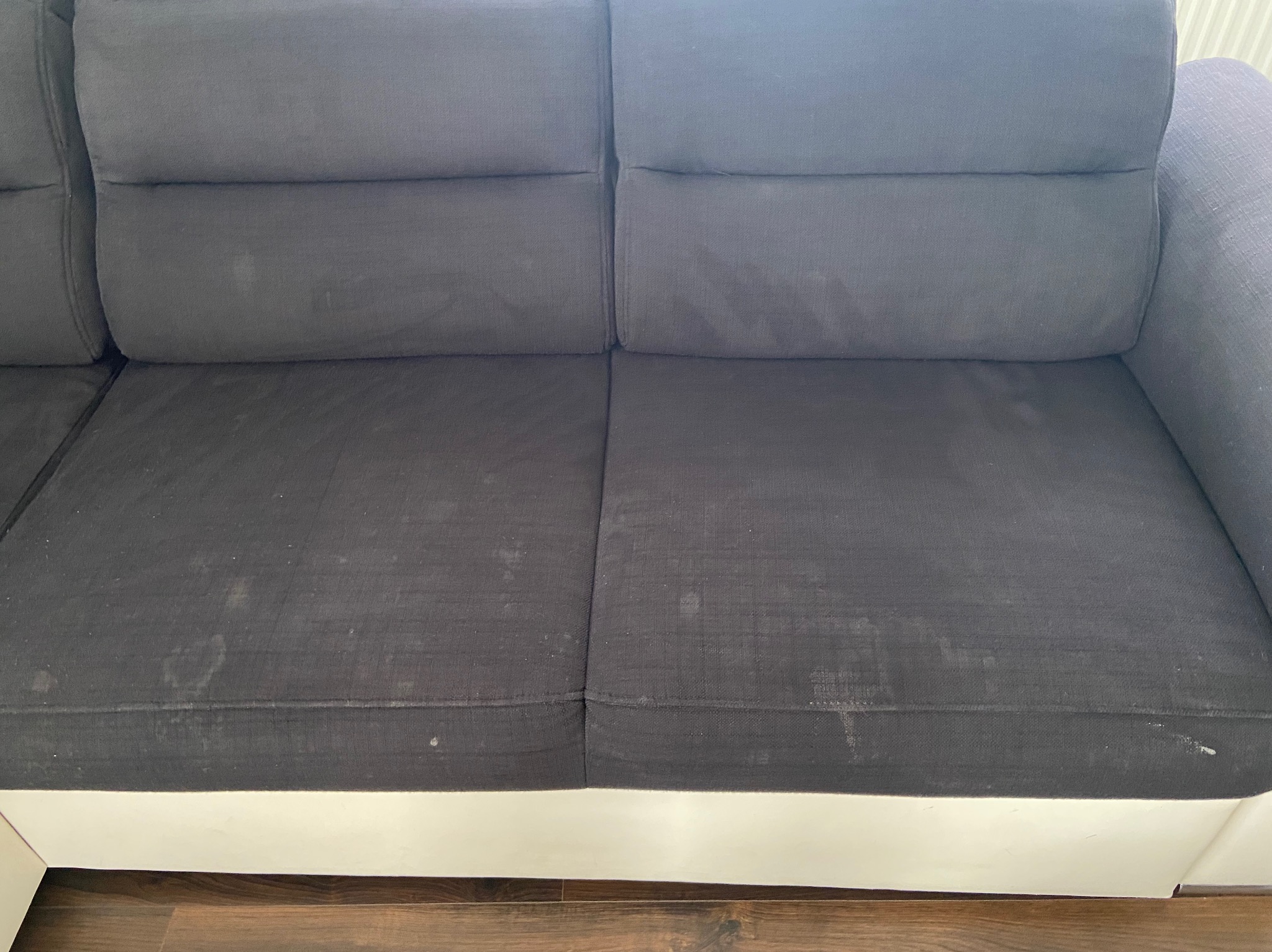 Szara sofa z widocznymi plamami na siedzisku, przed czyszczeniem, na tle drewnianej podłogi.