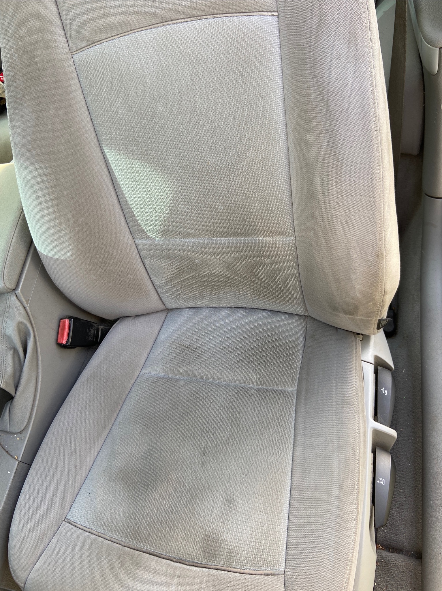 Szare, materiałowe siedzenie samochodowe z widocznymi plamami i zabrudzeniami, ukazujące potrzebę odświeżenia tapicerki.