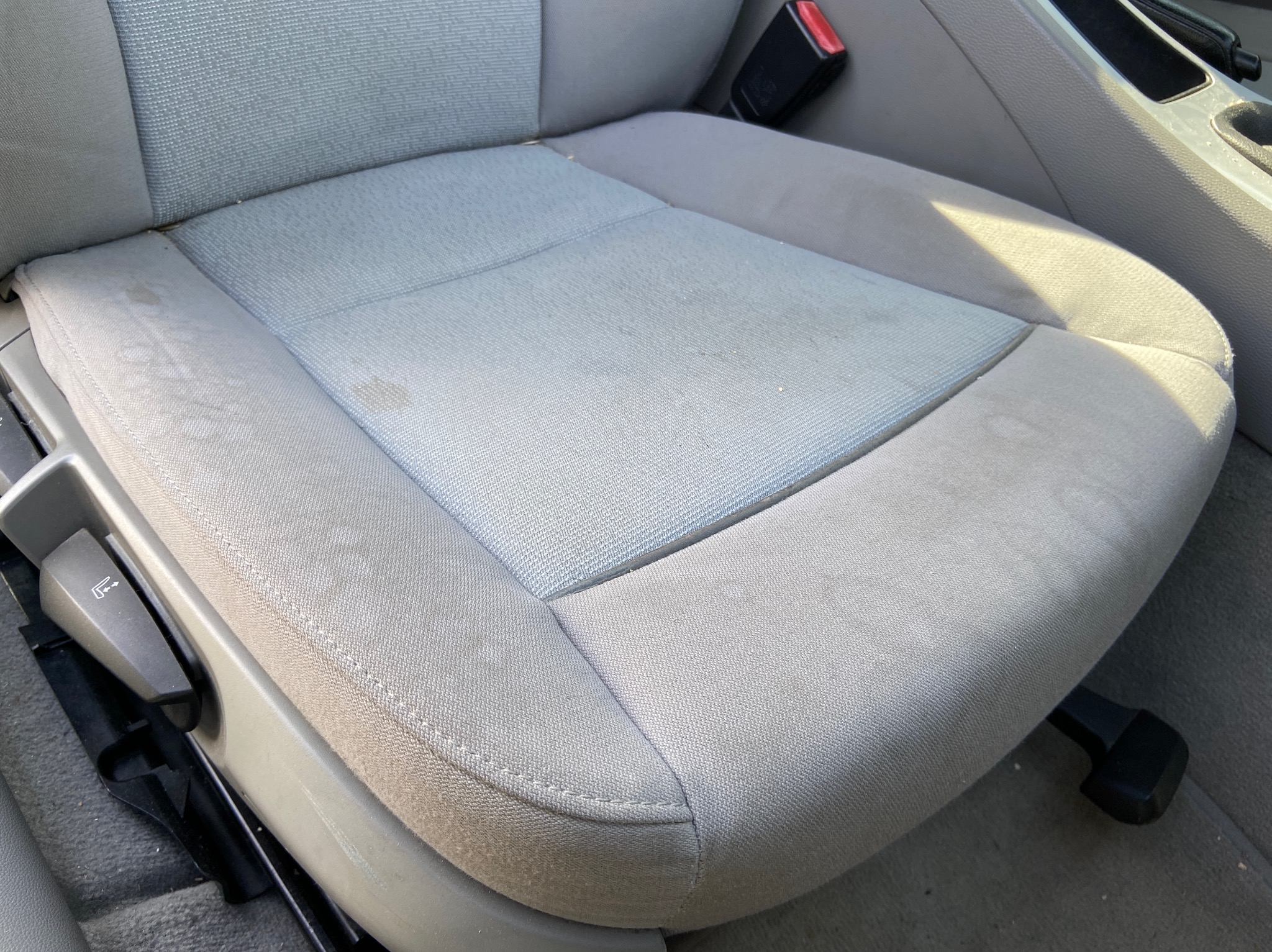 Szare samochodowe siedzenie z materiałową tapicerką, widoczne plamy i zabrudzenia przed czyszczeniem.