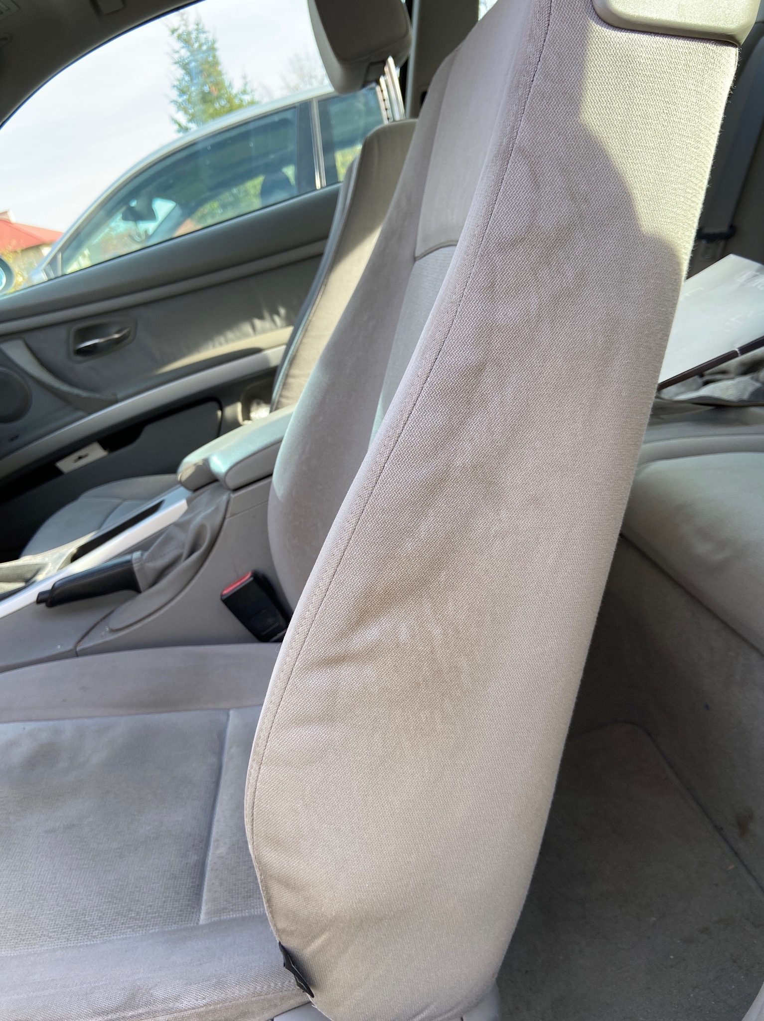 Szary materiał fotela samochodowego z widocznymi zabrudzeniami, uchwycony z bliska wewnątrz pojazdu.