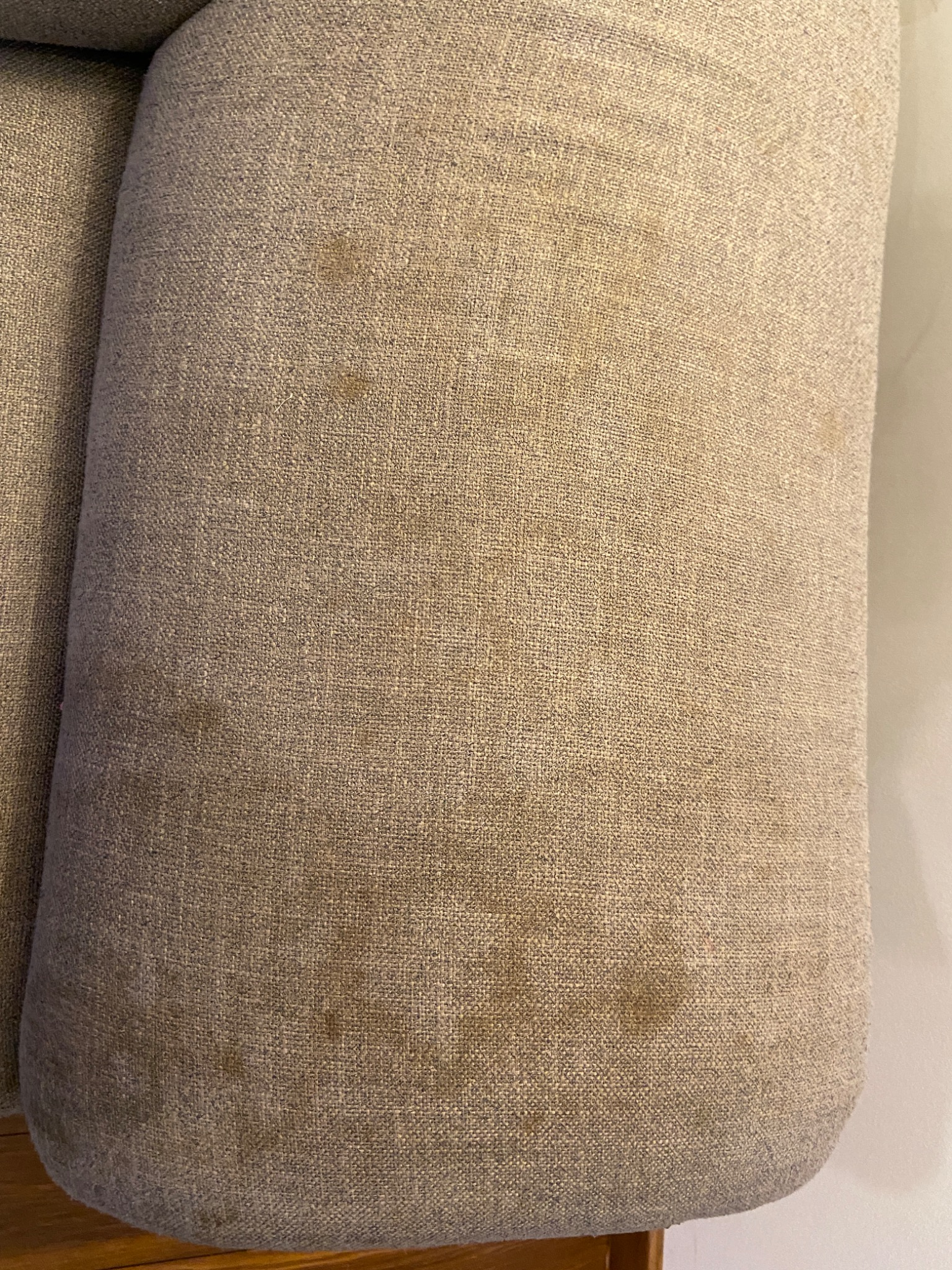 Fragment sofy z beżową tapicerką, widoczne plamy na materiale i wyraźna faktura tkaniny.