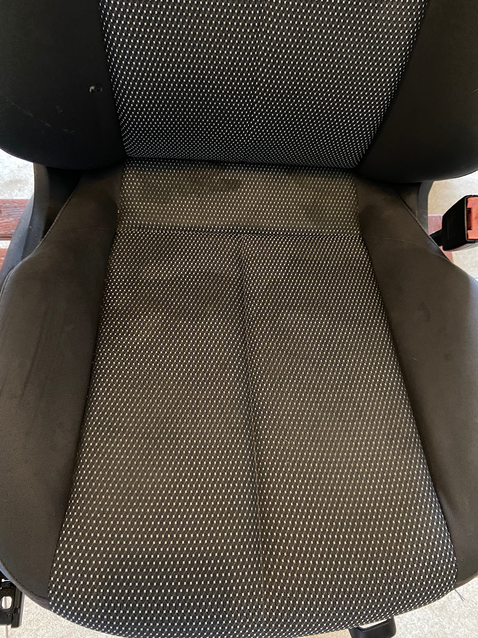 Czarny fotel samochodowy z tapicerką w drobny, biały wzór, widoczne plamy i zabrudzenia przed czyszczeniem.