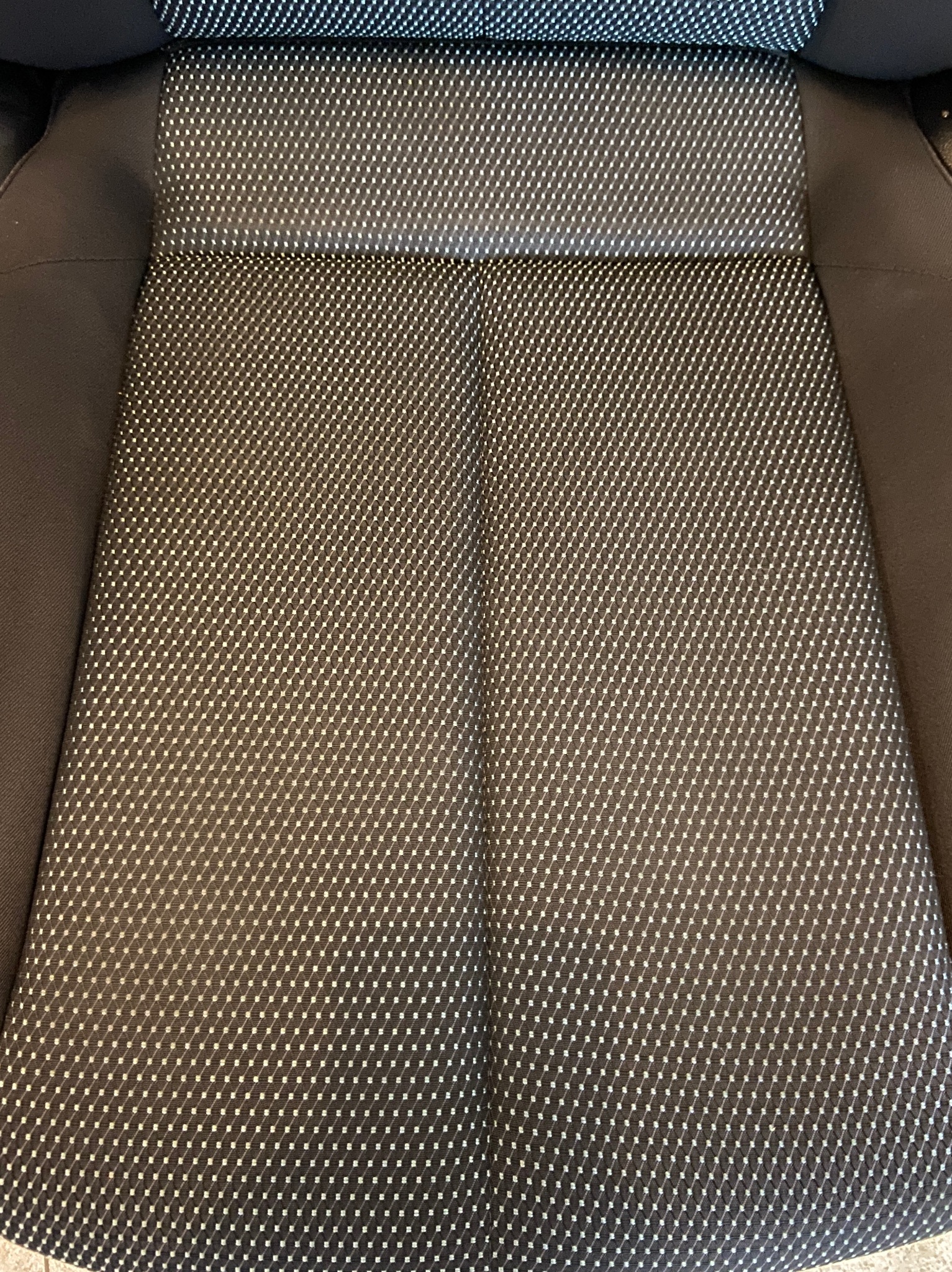 Wnętrze samochodu: czarno-szare siedzenie z drobnym wzorem w romby, widoczne z góry, z ciemną, gładką tapicerką po bokach.