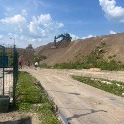 Kruszer-Warka Wioleta Gwiazda - Prace ziemne w toku: koparka na szczycie usypanego wzniesienia, pracownicy w terenie, widoczna waga najazdowa. Błękitne niebo z chmurami w tle.