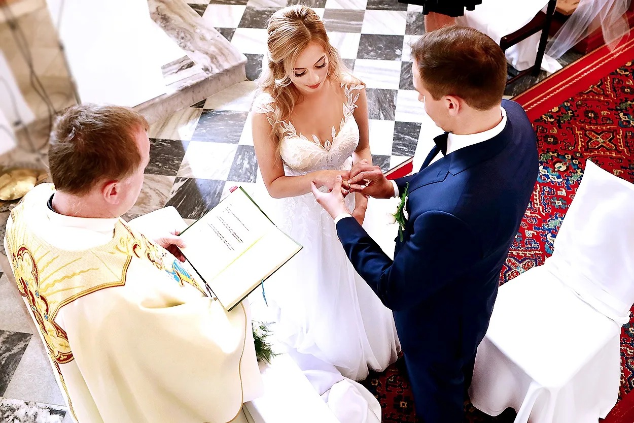 Wrocław: Moment zakładania obrączki podczas ceremonii ślubnej w kościele, z widocznym księdzem czytającym z księgi.