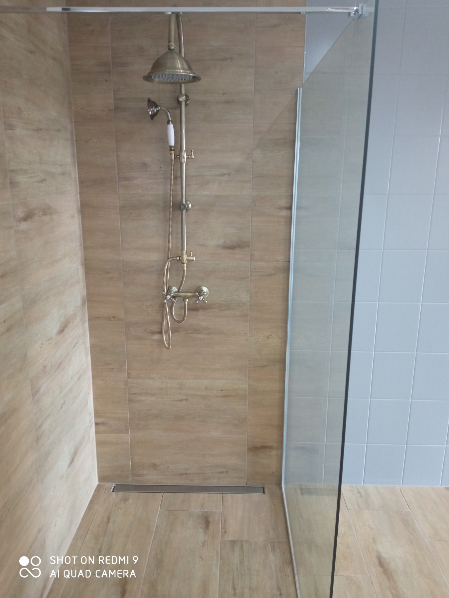 Kabina prysznicowa walk-in z deszczownicą w stylu retro, wykończona płytkami imitującymi drewno, z odpływem liniowym.