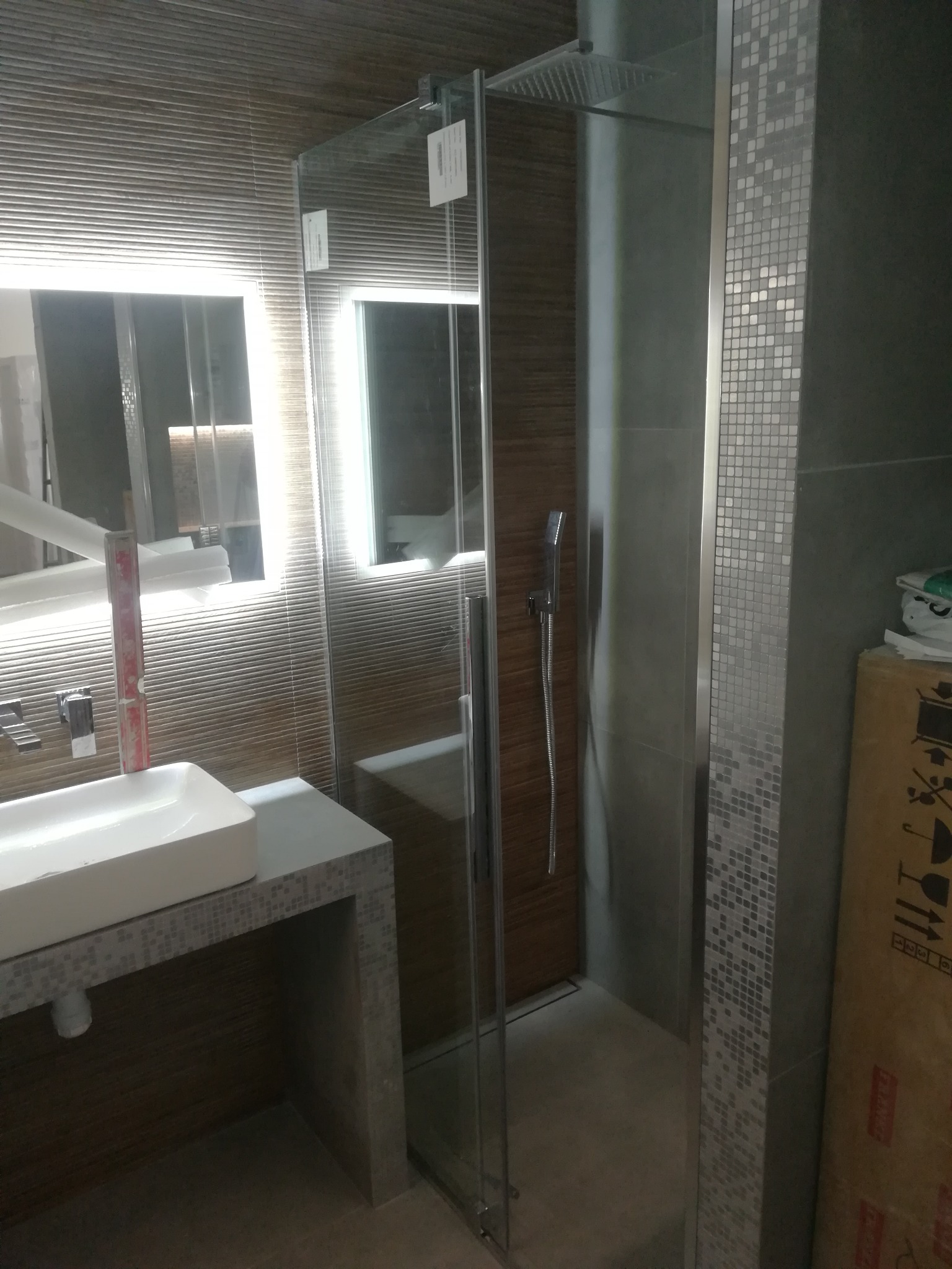 Nowoczesna łazienka z umywalką nablatową na blacie z mozaiki, kabina prysznicowa typu walk-in z deszczownicą i podświetlanym lustrem.