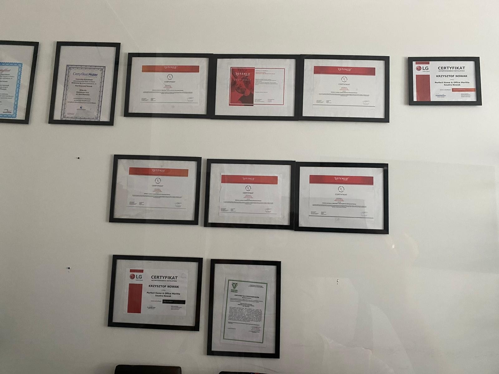 Ściana z powieszonymi certyfikatami w czarnych ramkach różnych firm, w tym certyfikat LG dla Krzysztofa Nowaka i certyfikaty Rotenso.