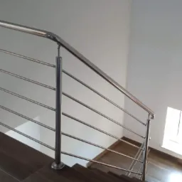 Polerowana, metalowa barierka schodowa z poziomymi prętami i mocowaniem do drewnopodobnych płytek schodowych, widok z góry.