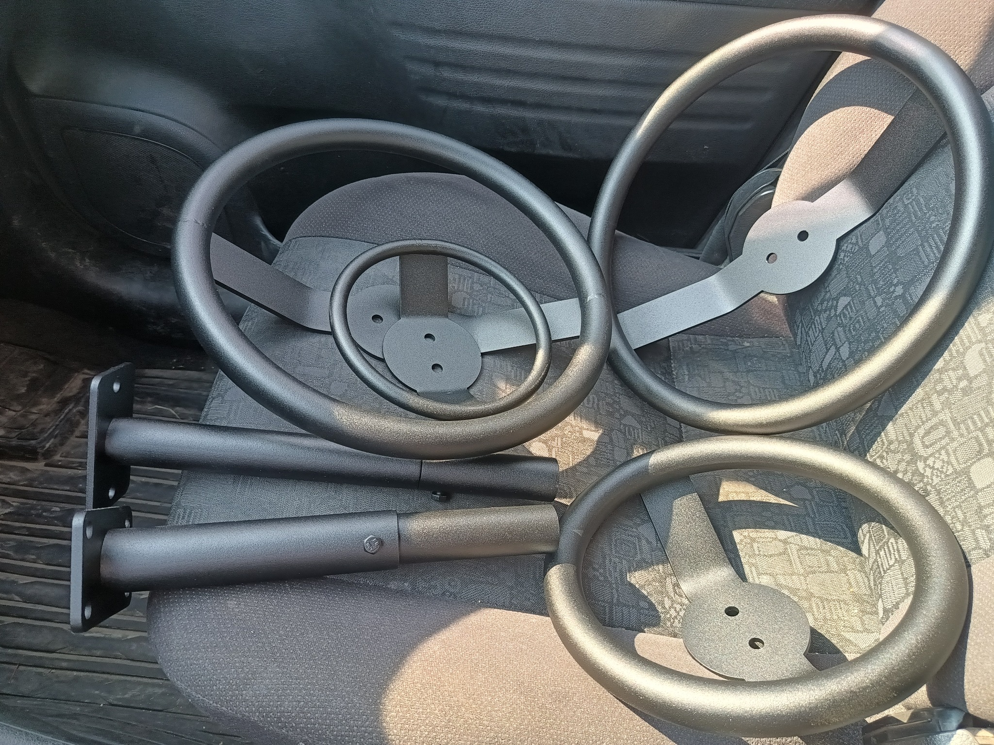 Elementy metalowe do konstrukcji: okrągłe uchwyty z mocowaniami oraz rury z flanszami, prawdopodobnie do balustrady lub poręczy, leżące na siedzeniu samochodowym.