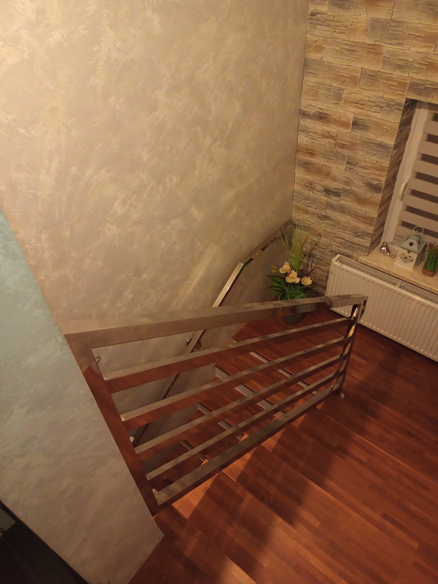 Wewnętrzne schody z drewnianymi stopniami i nowoczesną balustradą z poziomych, metalowych prętów, widok z góry, dekoracyjna ściana z kamienia obok okna.