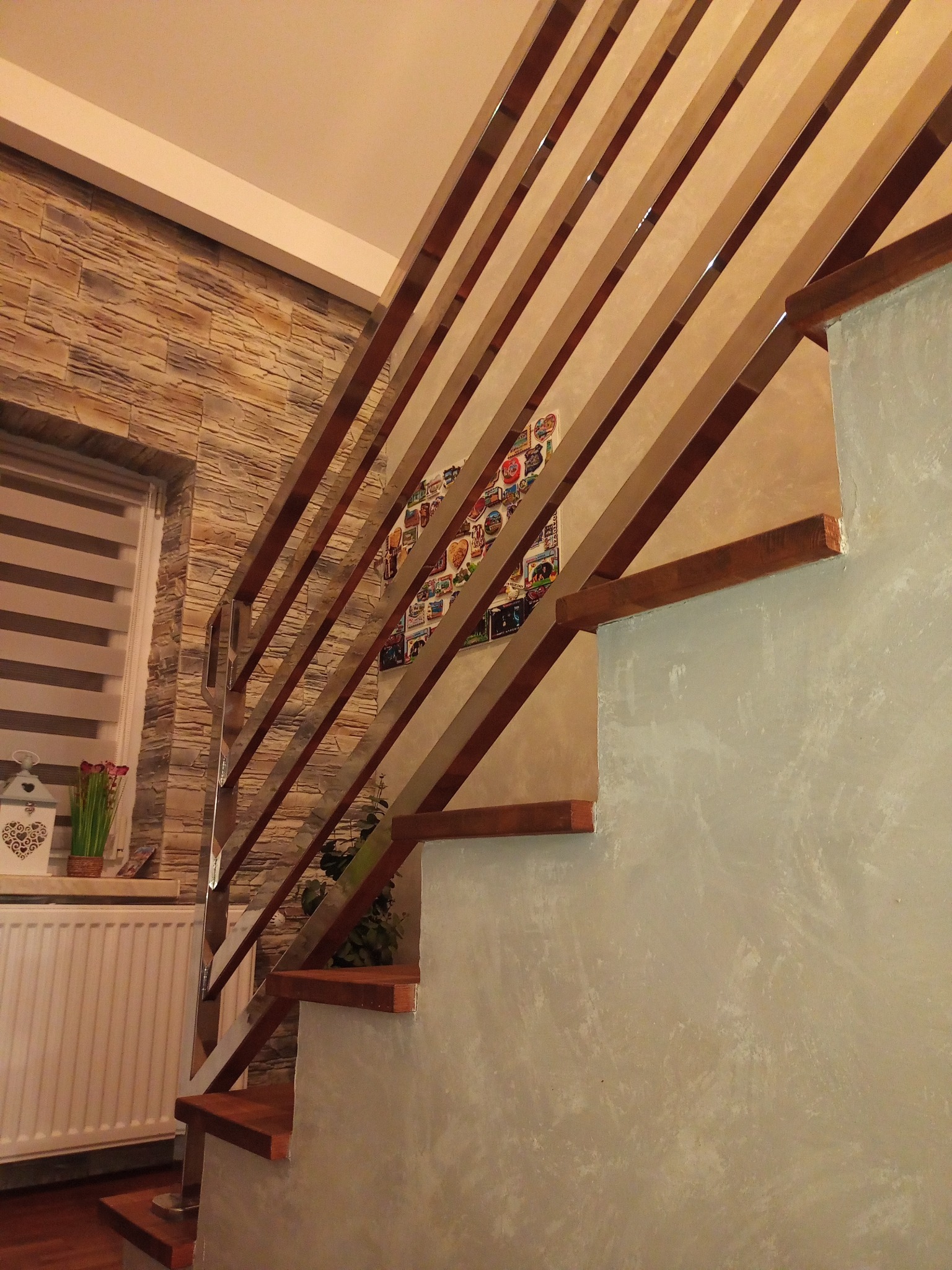 Schody drewniane z balustradą ze stali nierdzewnej, widok z dołu, na ścianie dekoracyjna tapeta i obrazek.