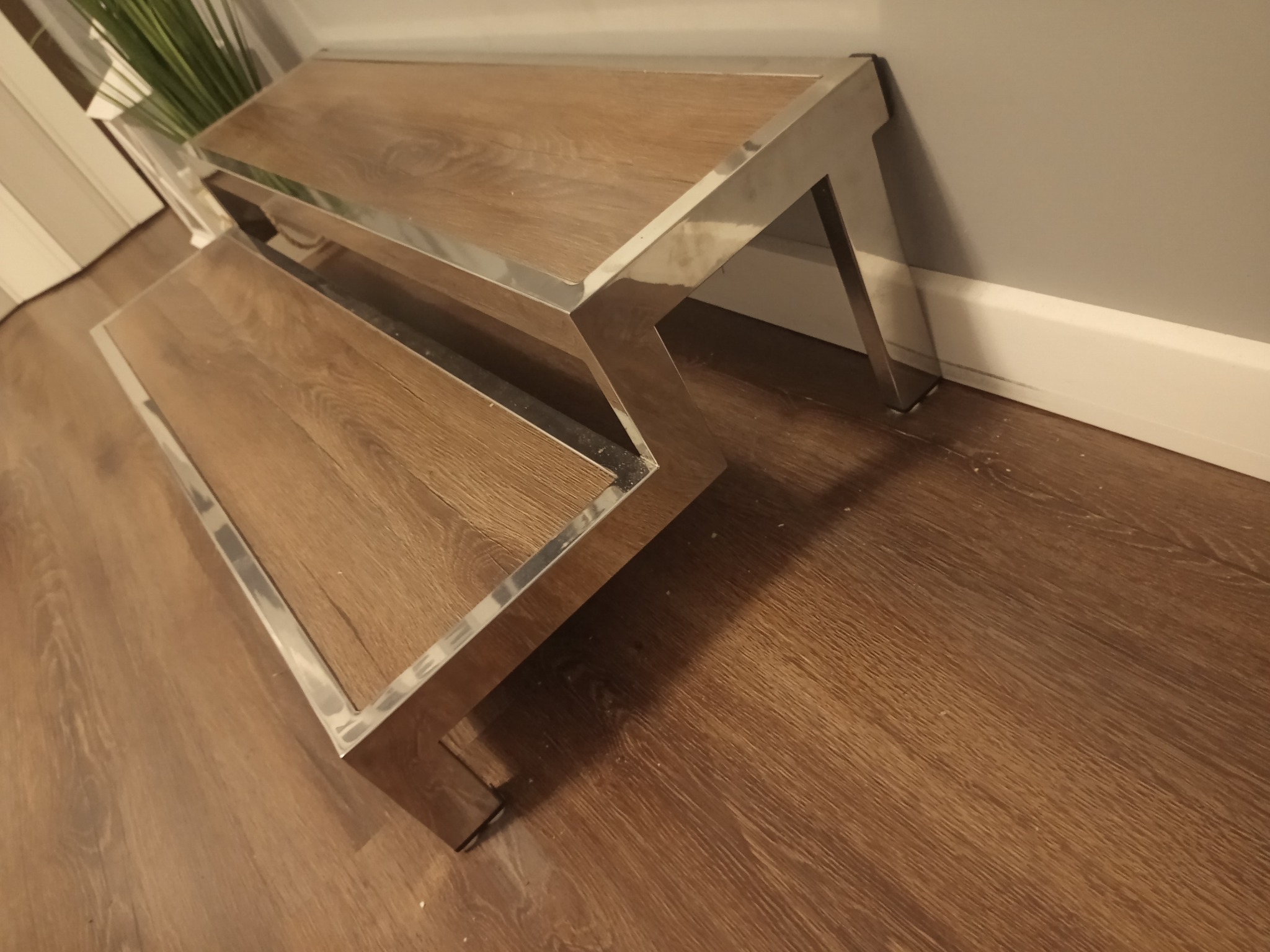 Dwustopniowy podest z drewnianymi stopniami i ramą ze stali nierdzewnej, ustawiony na drewnianej podłodze w pomieszczeniu.