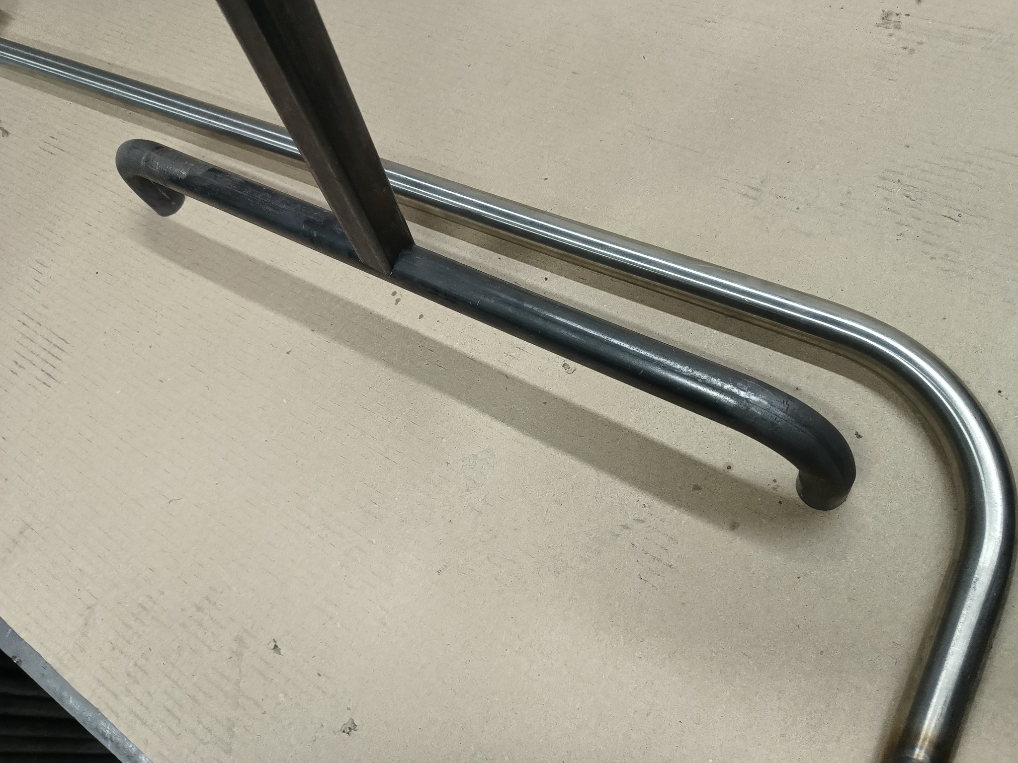 Metalowe elementy konstrukcyjne: spawana rama z profili zamkniętych i gięta rura nierdzewna. Elementy przygotowane do dalszej obróbki.