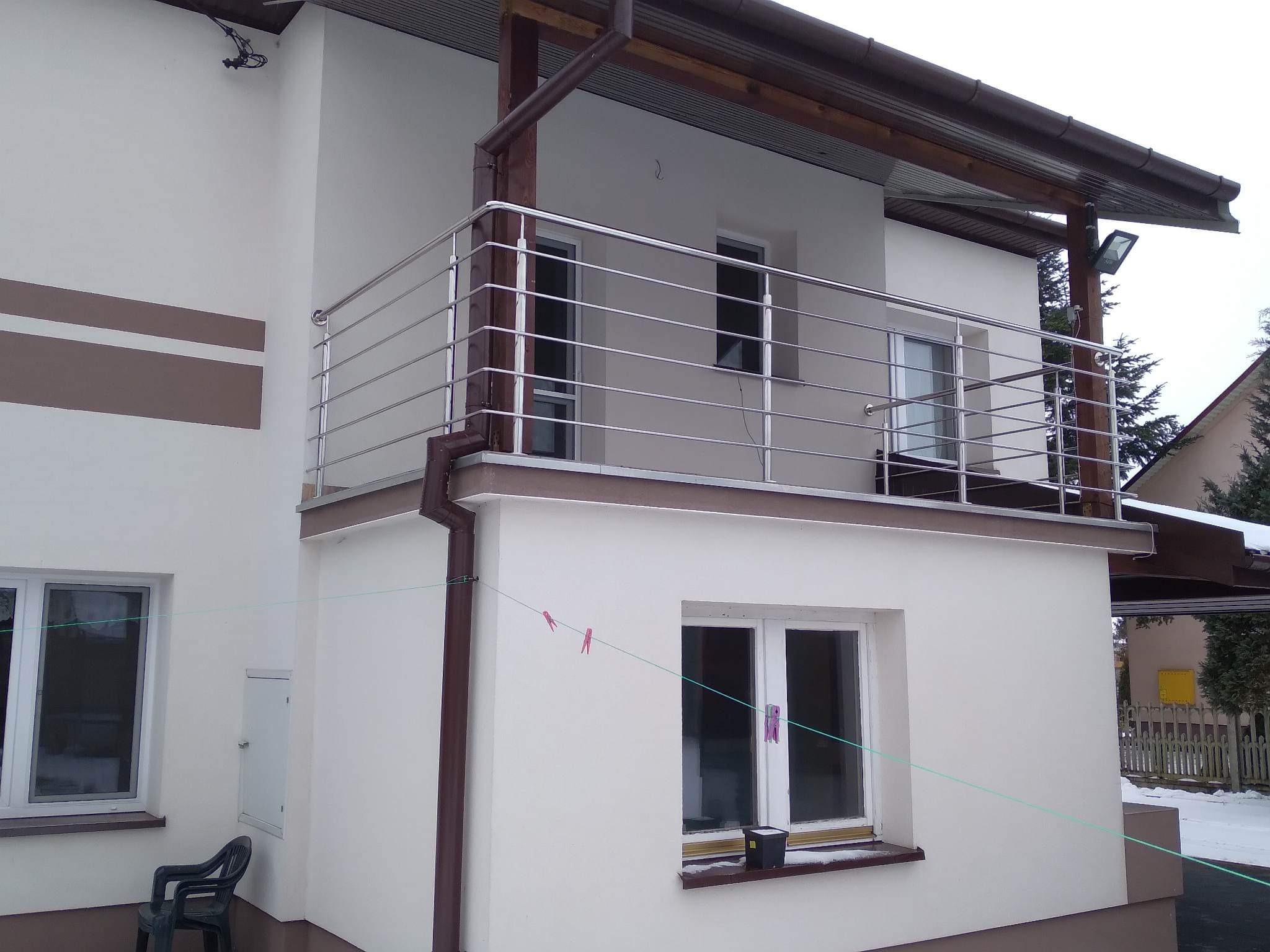 Balkon z nowoczesną, poziomą balustradą ze stali nierdzewnej, widoczny z zewnątrz budynku z elementami wykończenia w kolorze brązowym.