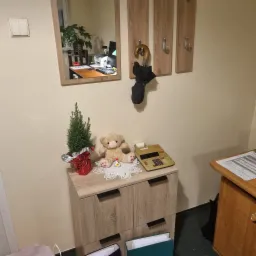 Biuro z elementami dekoracyjnymi: choinka w czerwonym opakowaniu, pluszowy miś z serduszkami, kalkulator Citizen, na szafce z szufladami, w tle lustro odbijające biurko i komputer.