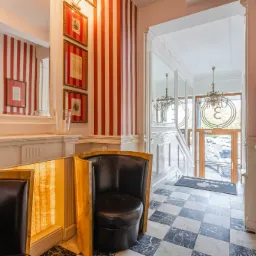 Hall z czarno-białą marmurową podłogą w szachownicę, krzesła klubowe z czarnej skóry, ściany w czerwono-białe pasy i lustra.