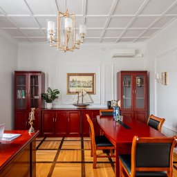 Kancelaria Adwokacka Adwokat Patryk Skalski - Eleganckie wnętrze gabinetu z mahoniowymi meblami, parkietem w szachownicę i dekoracyjnym oświetleniem. Na biurku laptop i statuetka Temidy.