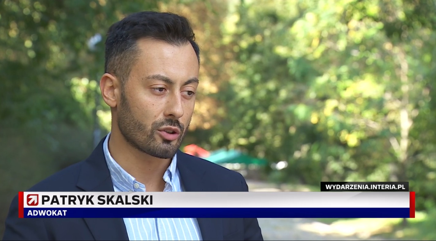 Portret mężczyzny w garniturze, z nazwiskiem i stanowiskiem 'Adwokat' w dolnej części ekranu, na rozmytym tle zieleni.