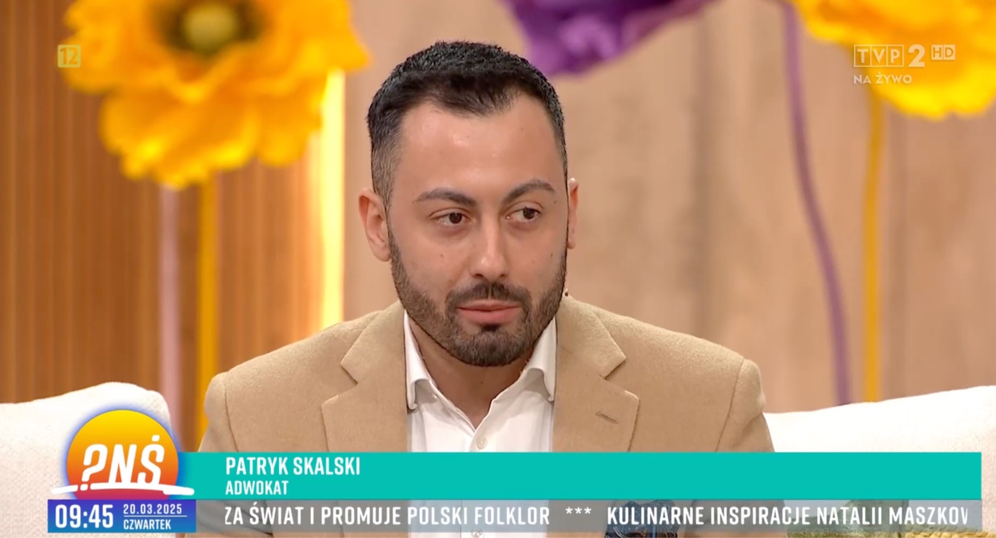 Portret adwokata Patryka Skalskiego w studiu telewizyjnym podczas programu na żywo, w tle kwiatowe dekoracje i logo stacji TVP2.