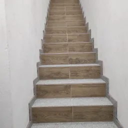 Schody wyłożone płytkami imitującymi drewno, z szarymi podstopnicami i cokolikami, widok z dołu w górę.