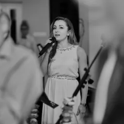 Czarno-białe zdjęcie wokalistki z mikrofonem podczas występu na żywo, w tle rozmyte postacie publiczności.