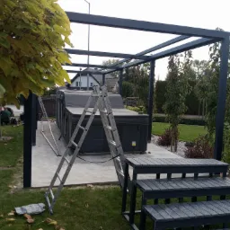 Montaż zadaszenia nad jacuzzi w ogrodzie, widoczne elementy konstrukcji, drabina i schodki z tworzywa sztucznego, trawnik z opadłymi liśćmi.