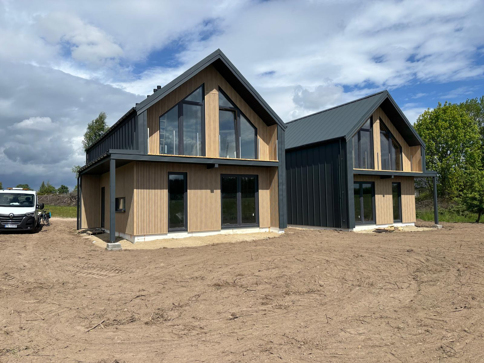 Dwa nowoczesne domy z drewnianą elewacją i dużymi oknami, widoczne z zewnątrz na tle pochmurnego nieba. Jeden dom zadaszony, drugi z elewacją z blachy.