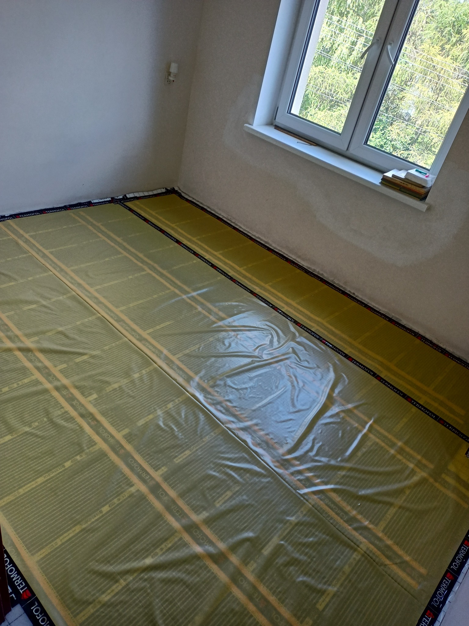 Rozłożone maty grzewcze marki Termofol na podłodze w pomieszczeniu z oknem, przygotowane do montażu ogrzewania podłogowego.
