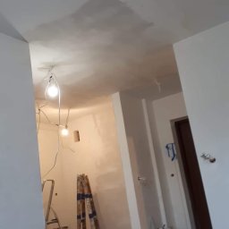 WOMEN'S TEAM PERFECT-BUD-CLEANING WIOLA&JOLA JOLANTA DOBROWOLSKA - Wnętrze w trakcie remontu: widoczne niedoskonałości na suficie po położeniu gładzi, przewody z żarówkami zwisające z sufitu, drabiny opierające się o ścianę, worki z gładzią gipsową na podłodze...