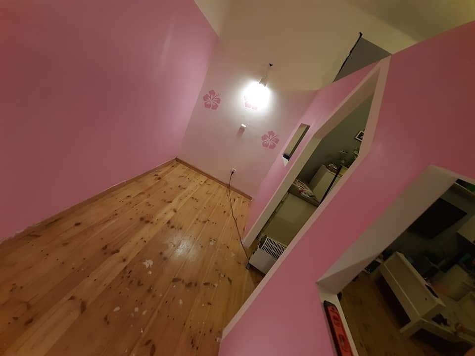 Pokój po malowaniu na różowo, z drewnianą podłogą i dekoracyjnymi kwiatami na ścianie, widok z nietypowej perspektywy.