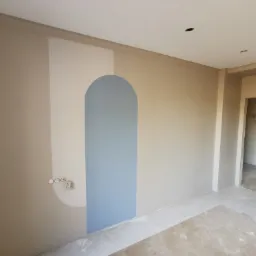 Wnętrze po odświeżeniu we Wrocławiu. Ściana z geometrycznym, niebieskim wzorem łuku, jasne kolory, widoczne gniazdka elektryczne i surowa podłoga.