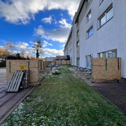 VANBLOK SPÓŁKA Z OGRANICZONĄ ODPOWIEDZIALNOŚCIĄ - Budowa hotelu w toku: widok na teren budowy z zabezpieczeniami, częściowo wykopany teren, przygotowania do fundamentów, budynek hotelowy w tle, pochmurne niebo.