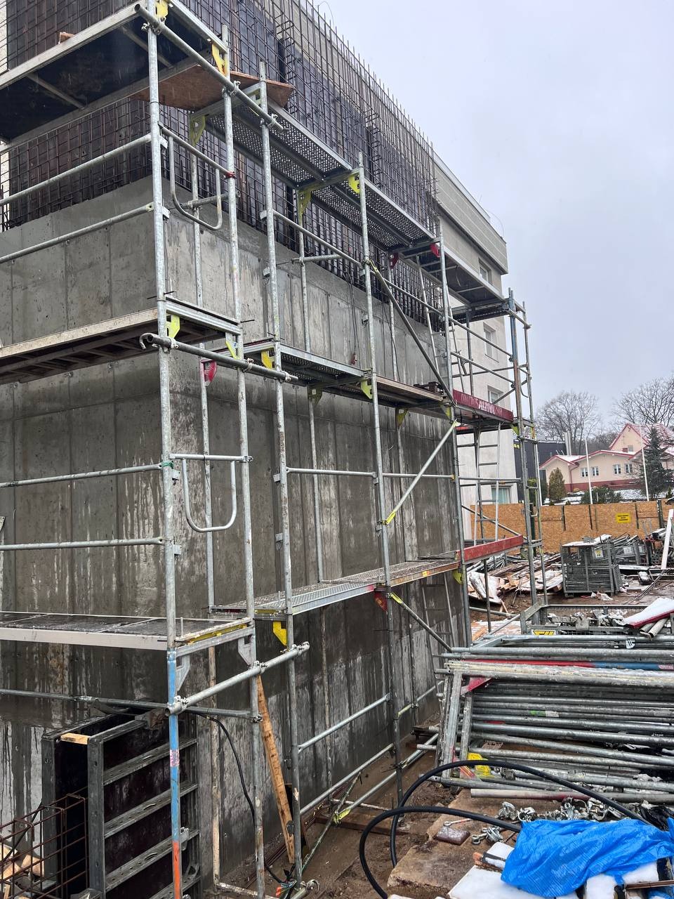 Betonowa konstrukcja budynku w trakcie budowy, widoczne rusztowania i zbrojenia. Surowy stan obiektu komercyjnego w pochmurny dzień.