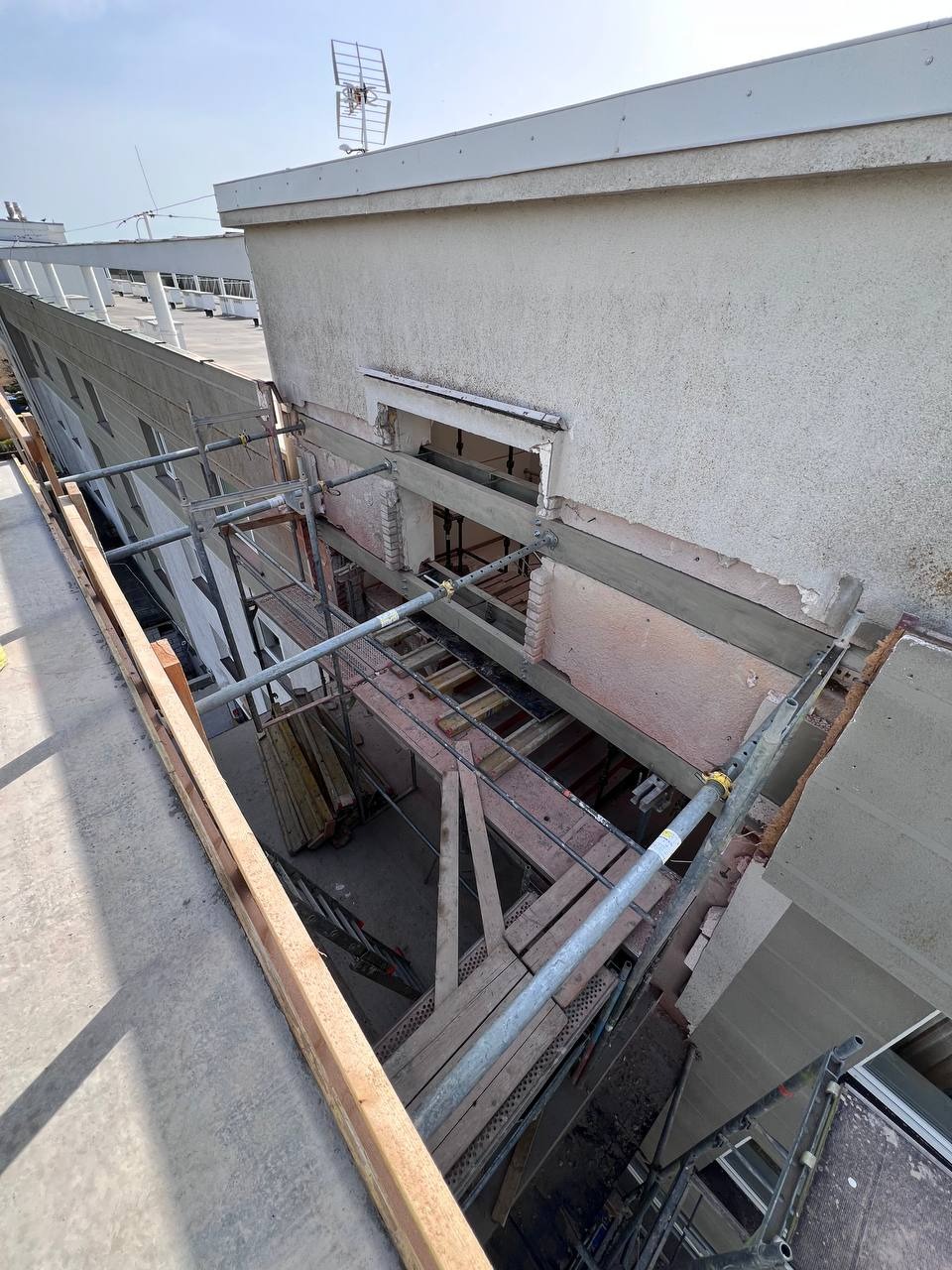 Wzmocnienie konstrukcji budynku komercyjnego w trakcie realizacji. Widoczne rusztowania, elementy konstrukcyjne i fragment elewacji. Ujęcie z góry.