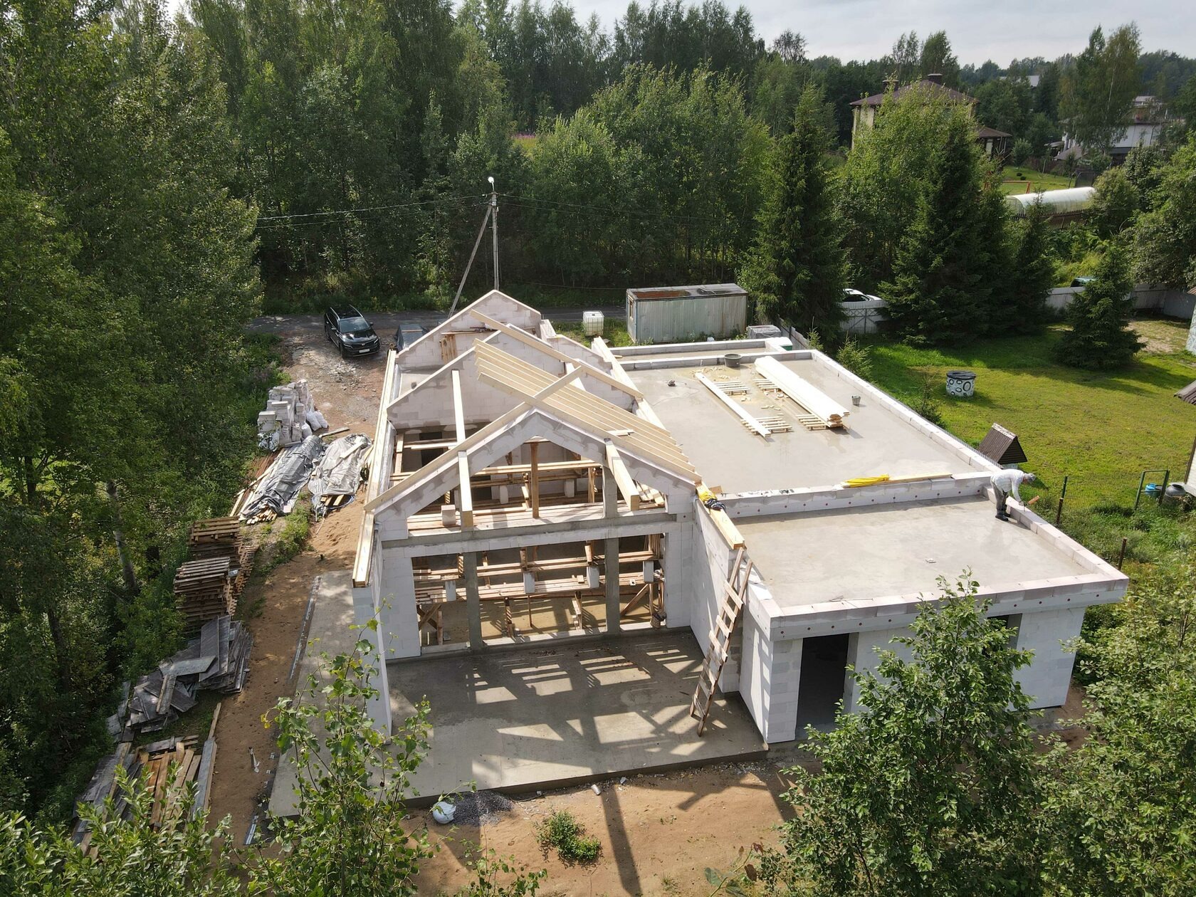 Budowa domu jednorodzinnego w stanie surowym otwartym z betonu komórkowego. Widok z góry na ściany, strop i konstrukcję dachu. Na dachu leżą deski.