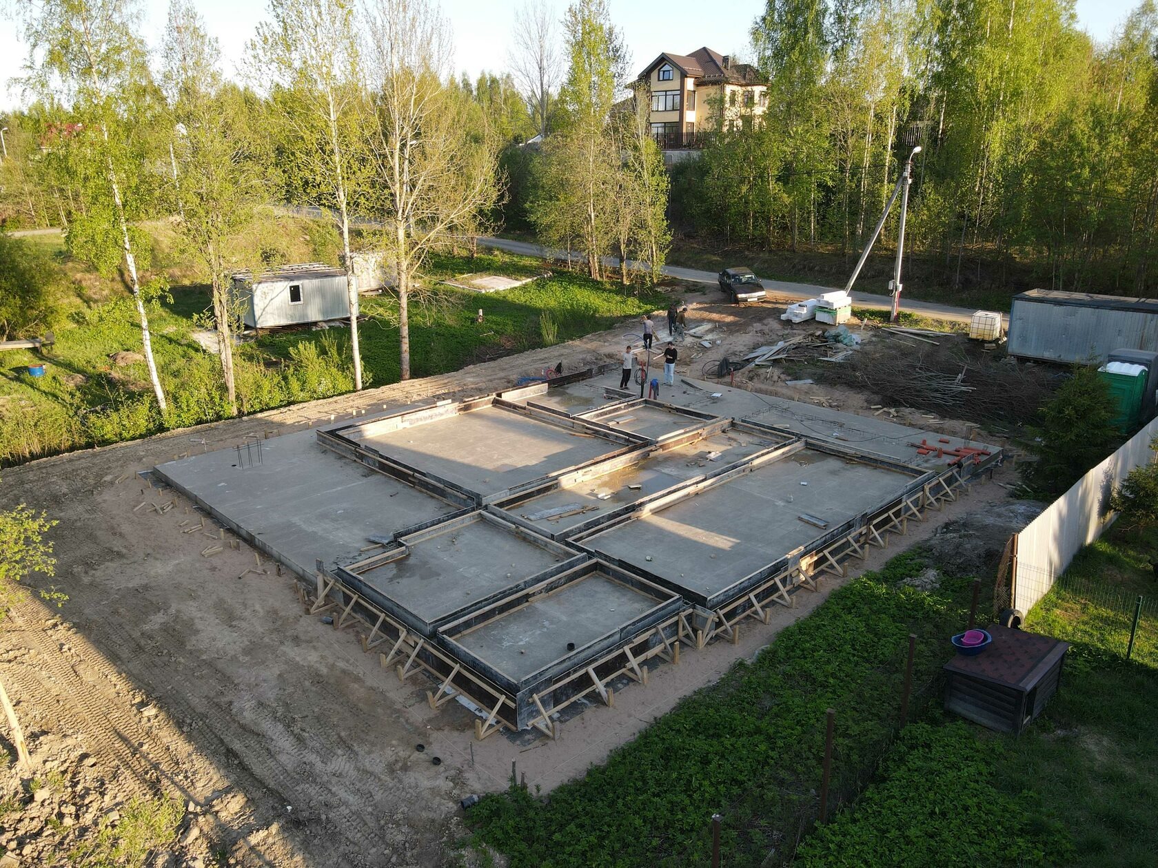 Zalany fundament pod dom jednorodzinny z widocznym szalunkiem i zbrojeniami, na tle zieleni i zabudowań. Ujęcie z góry, w słoneczny dzień.