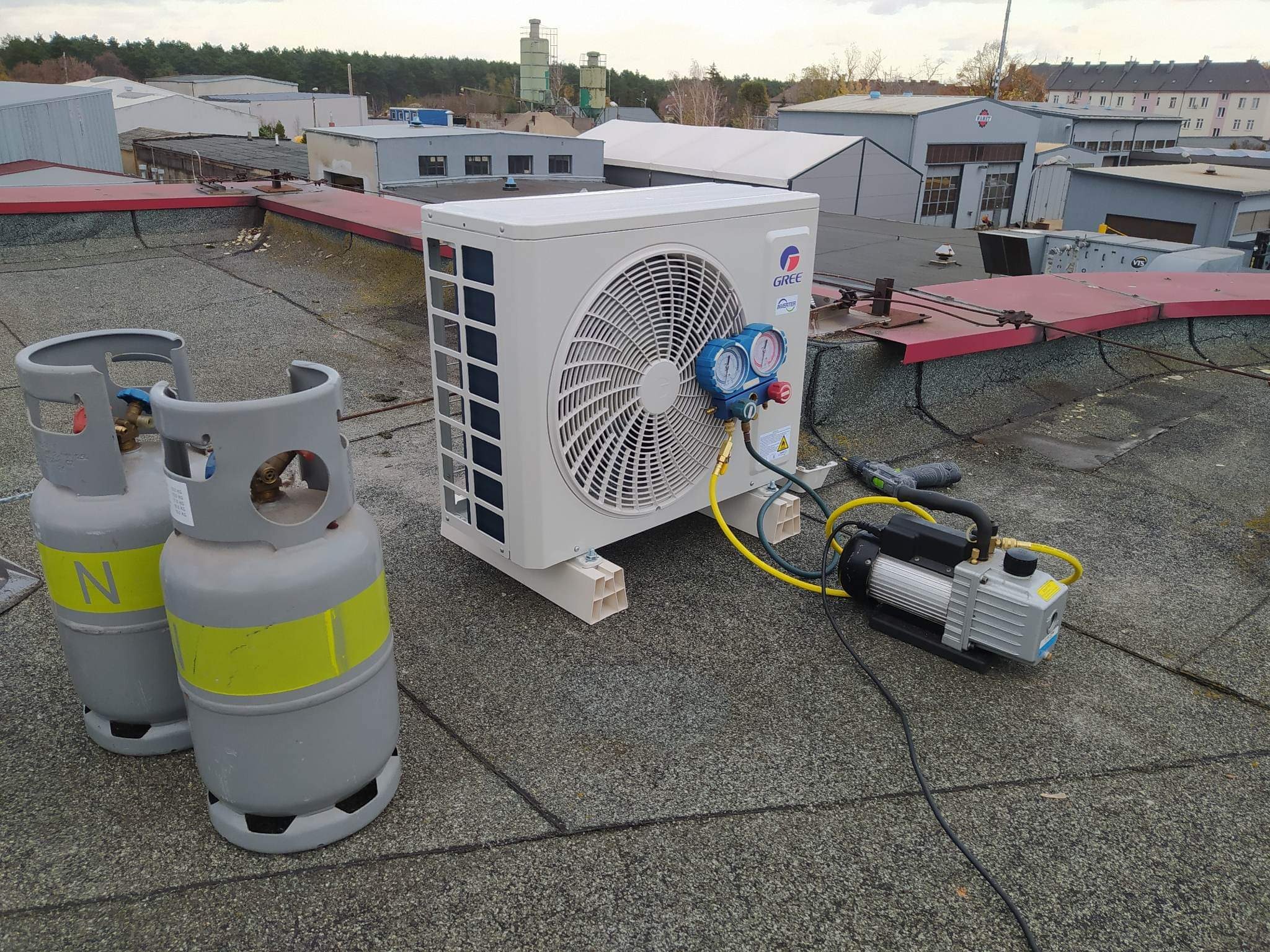 Montaż klimatyzatora GREE na dachu budynku w Bydgoszczy, widoczne butle z azotem, manometry i pompa próżniowa.