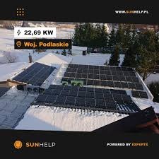 Panele słoneczne pokryte śniegiem na dachu budynku w Województwie Podlaskim, z widocznym logo Sunhelp w rogu. Instalacja o mocy 22,69 kW.