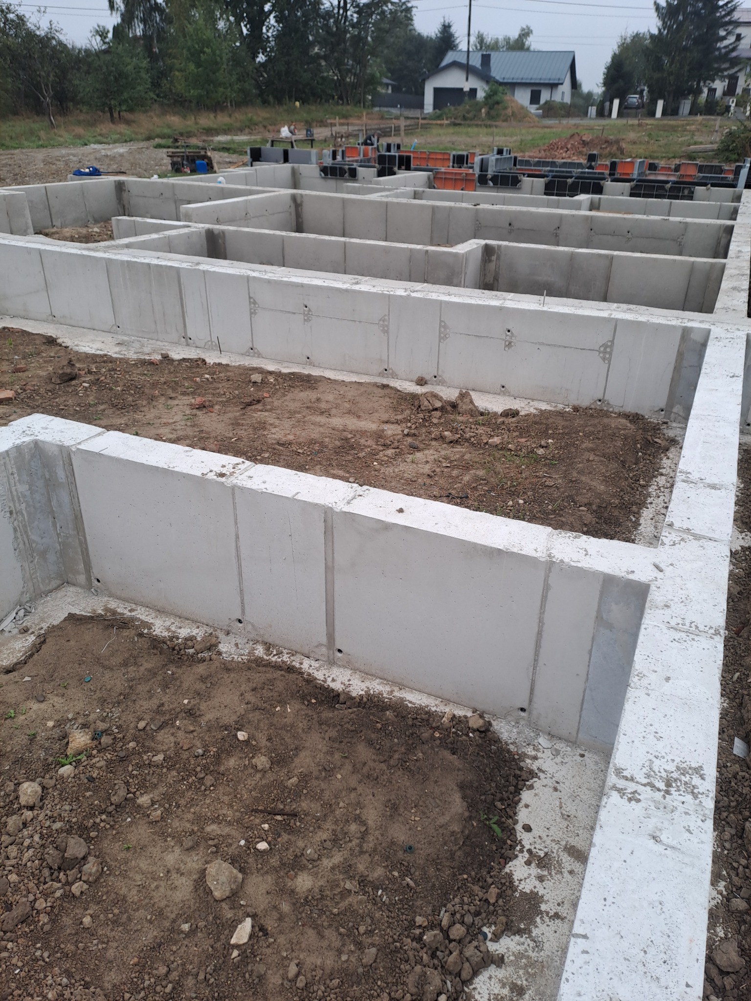 Zalane betonem ściany fundamentowe domu jednorodzinnego, widok z góry. Szalunki w tle. Surowy stan, wczesna faza budowy.