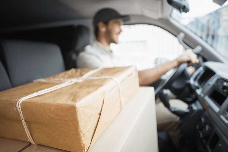 Kurier w trakcie jazdy samochodem dostawczym z paczką na siedzeniu pasażera, zabezpieczoną sznurkiem.