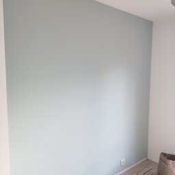 UWAGA!!Wykonanie gładzi,malowanie!i td... - Świeżo pomalowana ściana w odcieniu pastelowej zieleni, widoczne listwy przypodłogowe i torba papierowa w rogu pomieszczenia, gniazdko elektryczne na ścianie.