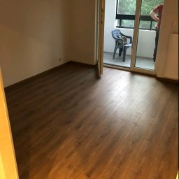 UWAGA!!Wykonanie gładzi,malowanie!i td... - Ułożony parkiet w pokoju z wyjściem na balkon, na którym stoi plastikowe krzesło, widoczne ściany pomalowane na biało.