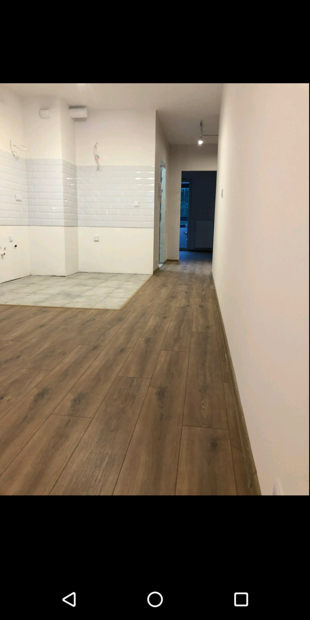 Ułożony parkiet w nowym mieszkaniu, widoczne płytki w części kuchennej, białe ściany i białe płytki w kuchni, surowe kable wystające ze ściany.