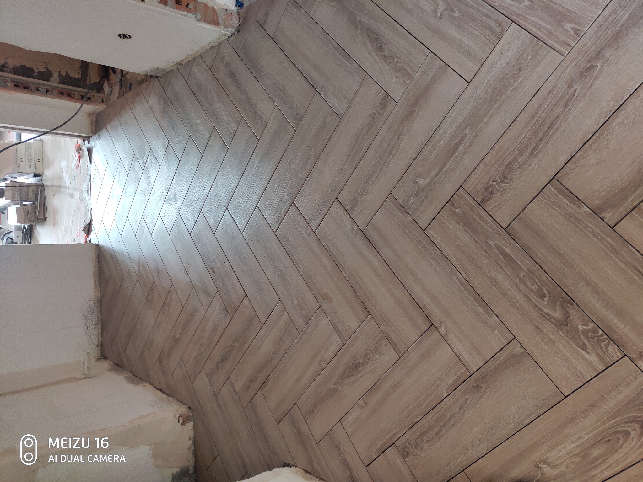 Ułożona pod kątem jodełki podłoga z płytek imitujących drewno, widoczne niedokończone ściany w tle.