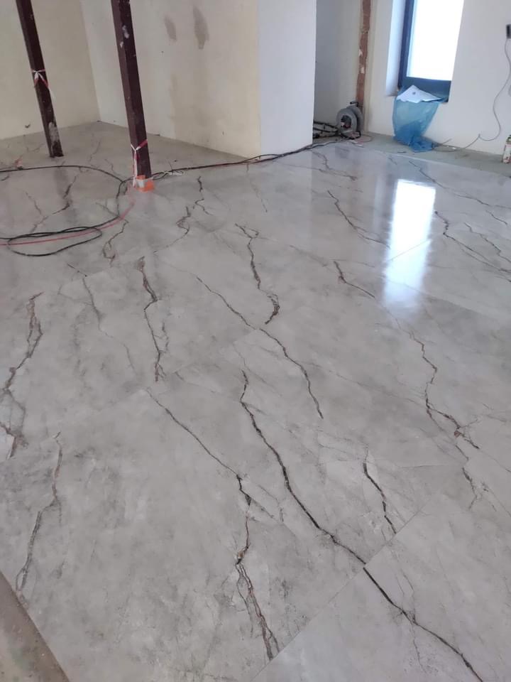 Ułożona podłoga z szarych płytek imitujących marmur z ciemnymi żyłami w trakcie remontu, widoczne kable i niedokończone ściany.