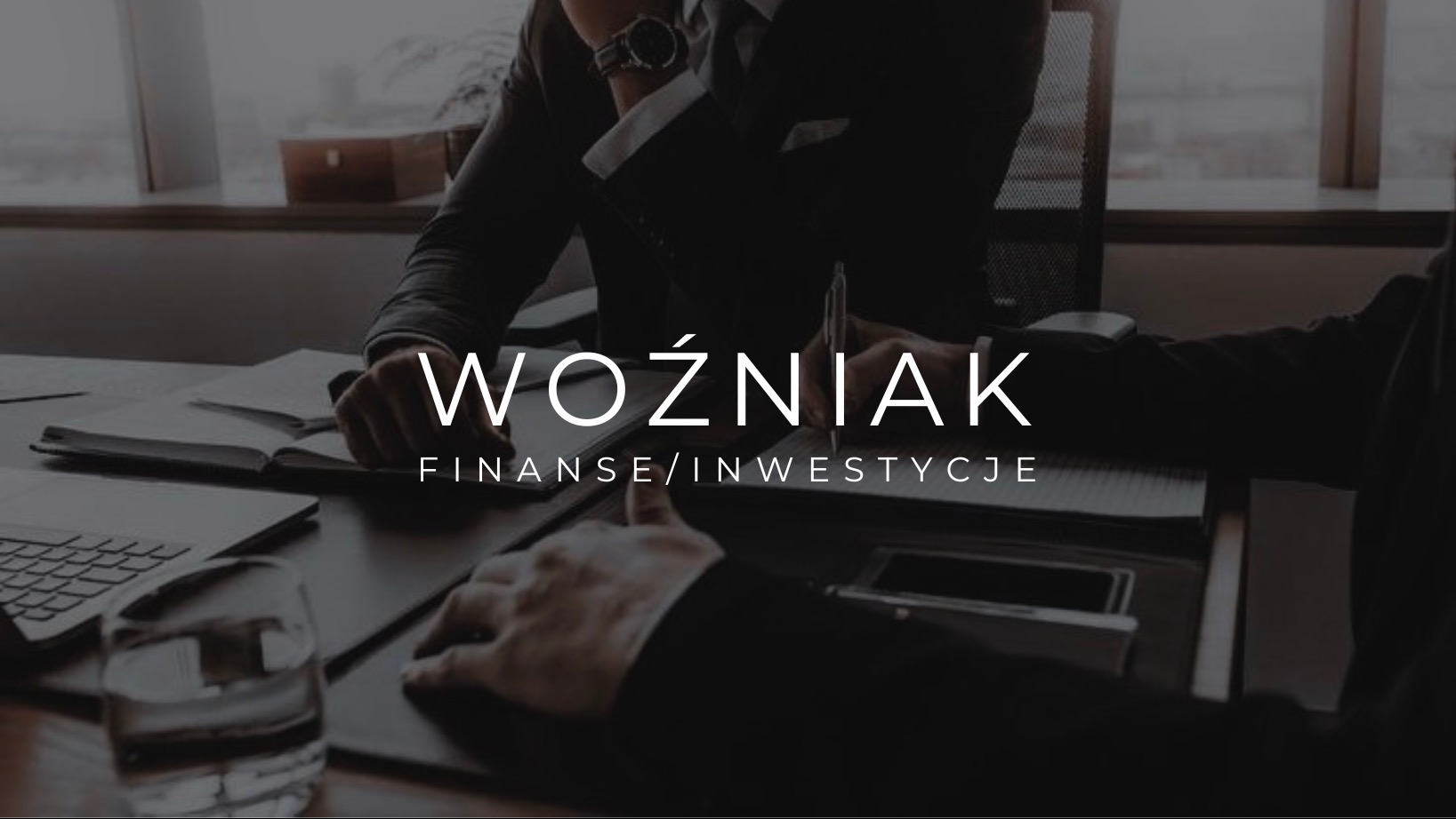 Dwóch mężczyzn w garniturach omawia dokumenty przy biurku, na którym leży laptop i szklanka wody, w tle okno; na pierwszym planie napis 'Woźniak Finanse/Inwestycje'.