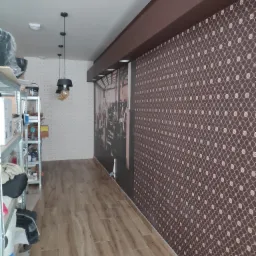 Wnętrze pomieszczenia z brązową ścianą w geometryczny wzór, drewnopodobną podłogą, wiszącymi lampami z żarówkami Edison i regałem magazynowym z lewej strony.