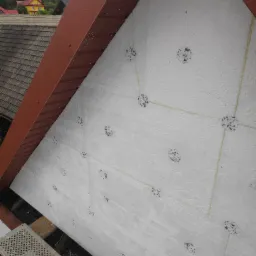 Ocieplenie szczytu dachu wełną mineralną, widoczne kołki mocujące i sznurki wyznaczające podział na segmenty, z rusztowaniem w dolnej części kadru.