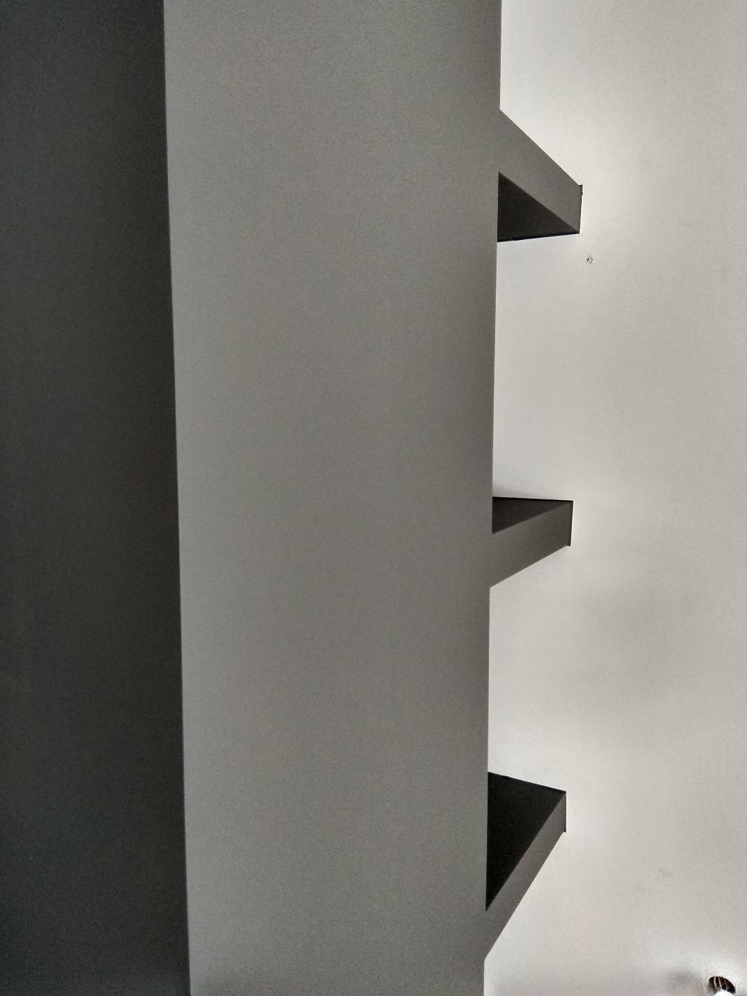 Ściana po nałożeniu gładzi w odcieniach szarości, z widocznymi półkami wbudowanymi w ścianę, z delikatnym światłem padającym na strukturę powierzchni.